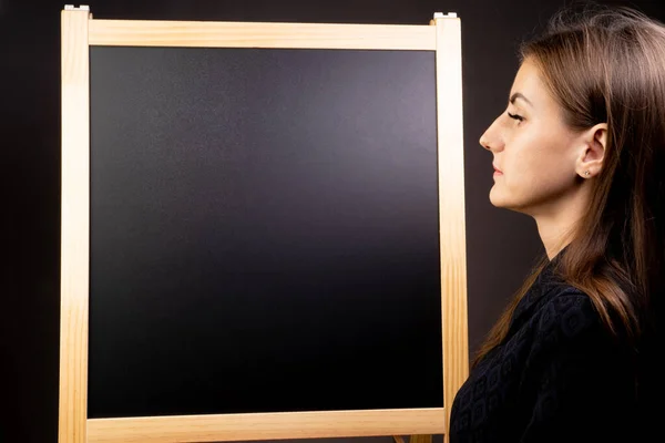 Female looks at an empty blackboard on which you can draw with chalk and write notes. Copy space — Stockfoto