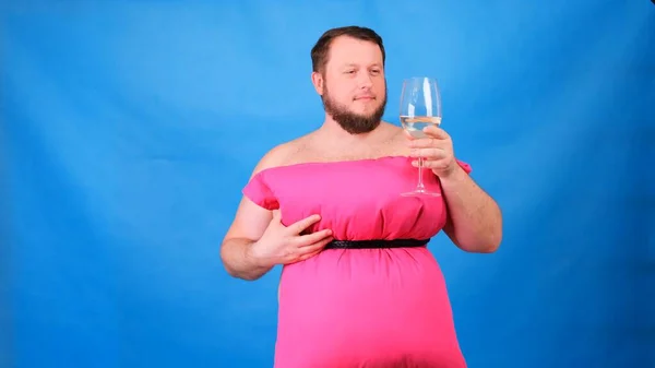 Cara barbuda engraçada em um vestido rosa feito de travesseiros bebe vinho de um copo em um fundo azul. Quarentena maluca. Moda 2020. Põe uma almofada. Desafio 2020 devido ao isolamento da casa — Fotografia de Stock