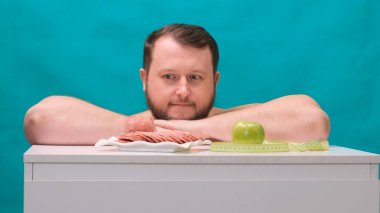 Sıradan tişörtlü çekici genç adam yeşil elma ve sosis arasında kolay bir seçim yapar. Sağlıksız fast food yerine sağlıklı organik meyveleri seçer, gözlerini kapatır ve neşeyle gülümser.