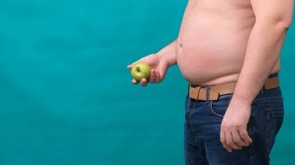 Dicker Mann mit dickem Bauch hält einen grünen Apfel in der Hand. Das Konzept der gesunden Ernährung und Abnehmen, Ernährung. — Stockfoto