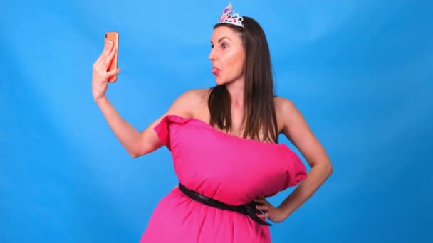 La muchacha más hermosa en el vestido rosado de las almohadas hace la selfie sobre el fondo azul. Cuarentena loca. Moda 2020. Ponte una almohada. Desafío 2020 debido al aislamiento de la casa — Vídeo de stock