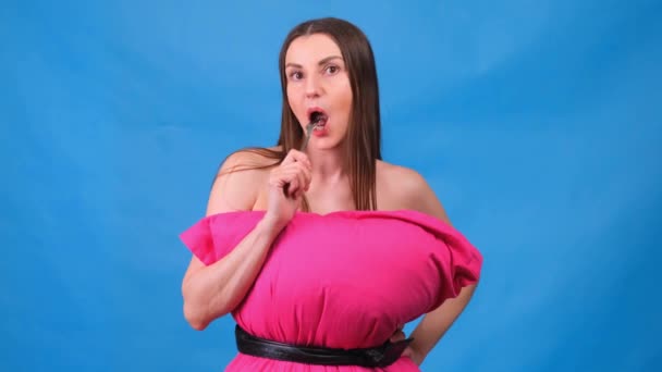La chica más hermosa en un vestido rosa hecho de almohadas está envolviendo un tenedor sobre un fondo azul. Cuarentena loca. Disfruta de la deliciosa comida. Moda 2020. Ponte una almohada. Desafío 2020 debido a casa — Vídeo de stock