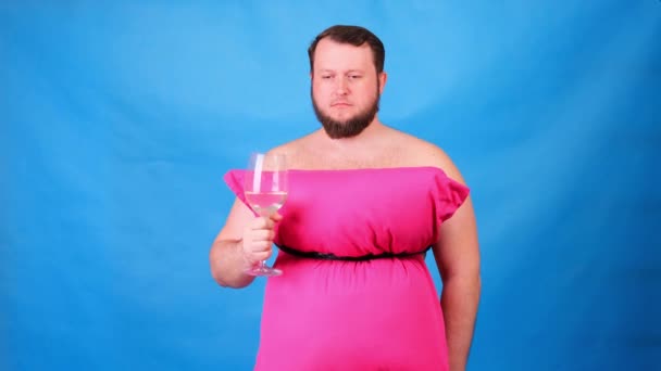 Αστείος μουσάτος με ροζ φόρεμα από μαξιλάρια πίνει κρασί από ποτήρι σε μπλε φόντο. Τρελή καραντίνα. Μόδα 2020. Βάλε ένα μαξιλάρι. Πρόκληση 2020 λόγω απομόνωσης των σπιτιών — Αρχείο Βίντεο
