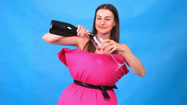 Das schönste Mädchen in einem rosafarbenen Kleid aus Kissen gießt Champagner in ein Glas auf blauem Hintergrund. Verrückte Quarantäne. Mode 2020. Auf ein Kissen legen. Herausforderung 2020 aufgrund der Isolation der Häuser. — Stockvideo