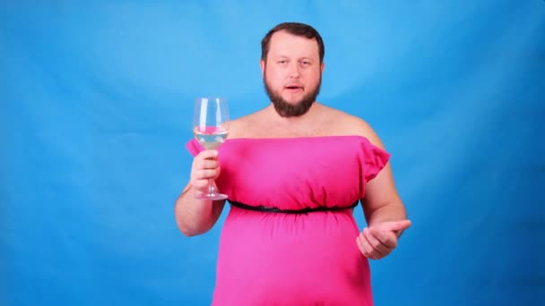 Funny bearded guy in a pink dress made of pillows drinks wine from a glass on a blue background. Crazy quarantine. Fashion 2020. Put on a pillow. Challenge 2020 due to house isolation — Stock Video