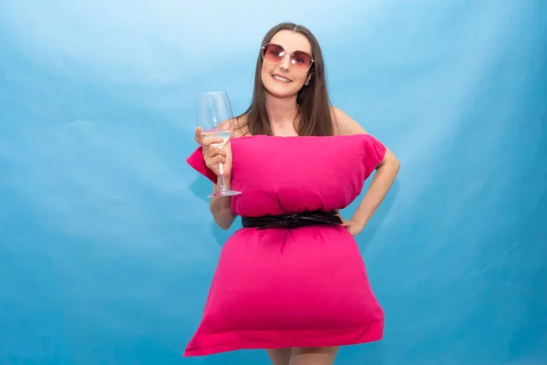 Ευτυχισμένη γυναίκα με ροζ μαξιλάρι φόρεμα και γυαλιά ηλίου κρατώντας ένα ποτήρι σαμπάνια σε ένα μπλε φόντο για την τρελή πρόκληση Pillow οφείλεται στην ύπαρξη στο σπίτι στην απομόνωση. Μοντέρνο κορίτσι. Μαξιλάρι κλήση λόγω — Φωτογραφία Αρχείου