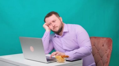 Erkek, iş yerinde dizüstü bilgisayarını özlüyor ve cips yiyor. Serbest konsept, evde çalışma, iş yorgunluğu, ilgisizlik.