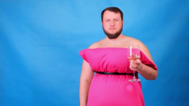 Divertente ragazzo barbuto in un abito rosa fatto di cuscini beve vino da un bicchiere su uno sfondo blu. Una quarantena pazzesca. Moda 2020. Mettiti un cuscino. Sfida 2020 a causa dell'isolamento della casa — Video Stock