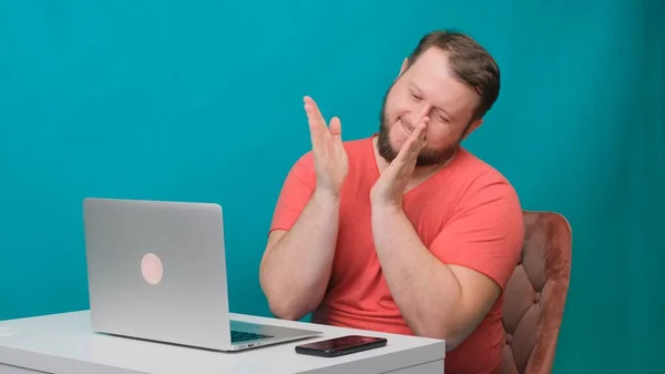 Young happy businessman in a pink t-shirt works on a laptop and claps his hands on a green screen. Portrait of a male talking man looking into his laptop. Man working at his desk in the office. — Stock Photo, Image