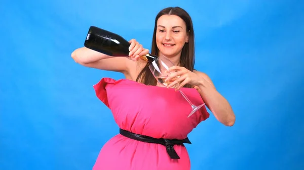 Het mooiste meisje in een roze jurk van kussens giet champagne in een glas op een blauwe achtergrond. Gekke quarantaine. Mode 2020. Leg een kussen op. Uitdaging 2020 als gevolg van huisisolatie. — Stockfoto
