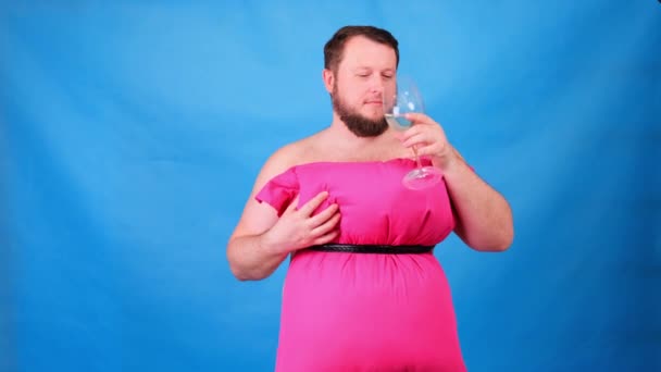 Vousáč v růžových šatech z polštářů pije víno ze sklenice na modrém pozadí. Šílená karanténa. Móda 2020. Dej si polštář. Výzva 2020 v důsledku izolace domu — Stock video