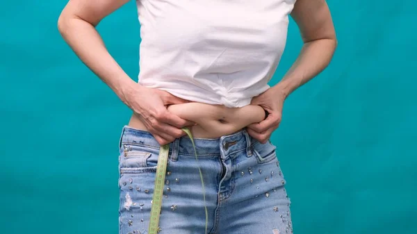 Frau hält eine Hautfalte auf einem dicken Bauch, fetter weiblicher Körper auf grünem Hintergrund. Kühne weibliche Taille. Das Konzept der Gewichtsabnahme und Ernährung. — Stockfoto