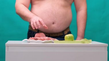 Koca göbekli bir adam sosis ve yeşil elma arasında seçim yapar. Diyet ve irade kavramı.