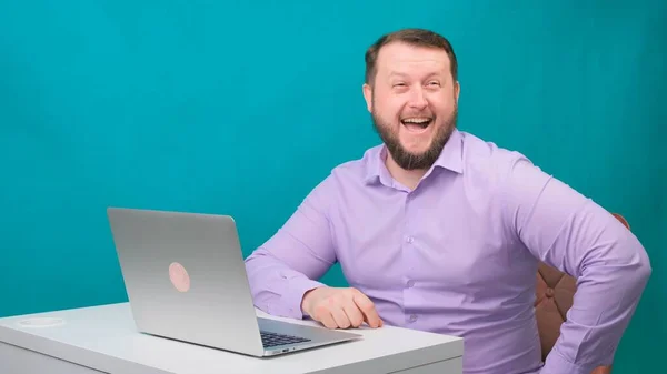 Joven hombre de negocios feliz sonriendo y hablar a la cámara. Retrato de un hombre riendo mientras mira su portátil. Hombre trabajando en su escritorio en la oficina — Foto de Stock