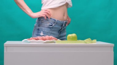 Kadın yeşil arka planda elma ya da sosis arasında seçim yapar. Sağlıklı beslenme, diyet ve irade kavramı.