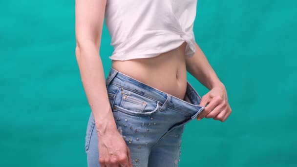 Atractiva mujer joven con pantalones vaqueros y mostrando cuerpo delgado después de entrenamientos deportivos y alimentación saludable. Concepto de pérdida de peso . — Vídeos de Stock