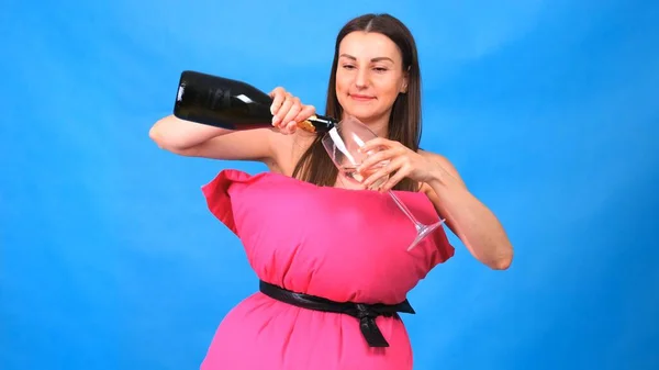 Το πιο όμορφο κορίτσι σε ένα ροζ φόρεμα από μαξιλάρια ρίχνει σαμπάνια σε ένα ποτήρι σε μπλε φόντο. Τρελή καραντίνα. Μόδα 2020. Βάλε ένα μαξιλάρι. Πρόκληση 2020 λόγω απομόνωσης των σπιτιών. — Φωτογραφία Αρχείου