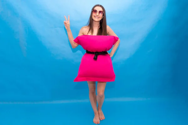 Χαριτωμένο γυναίκα σε ροζ μαξιλάρι φόρεμα πάνω από το μπλε φόντο για τρελό Pillow Challenge οφείλεται να μείνετε στο σπίτι απομόνωση. Καροναβιάρι Καραντίνα. Κορίτσι της μόδας. Μαξιλάρι κλήση λόγω μόνωση στο σπίτι. — Φωτογραφία Αρχείου