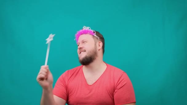 Leuke man met een baard in een roze T-shirt met een deadema op zijn hoofd droomt met een toverstaf in zijn hand. Een grappige tovenaar grap te maken en een wens te vervullen. — Stockvideo