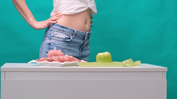 Vrouw kiest tussen appel of worst op een groene achtergrond. Het concept van een gezonde voeding, voeding en wilskracht. — Stockvideo