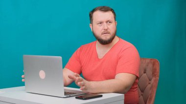 Pembe tişörtlü genç mutlu iş adamı laptopta çalışır ve yeşil ekranda kameraya konuşur. Dizüstü bilgisayarına bakan konuşan bir erkeğin portresi. Ofisteki masasında çalışan bir adam..