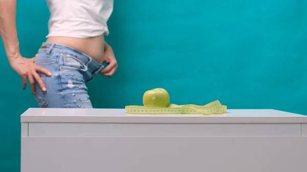 Θηλυκό λίπος κοιλιά και πράσινο μήλο στο προσκήνιο, επιλεκτική εστίαση. Η έννοια της απώλειας βάρους και της σωστής διατροφής. — Φωτογραφία Αρχείου
