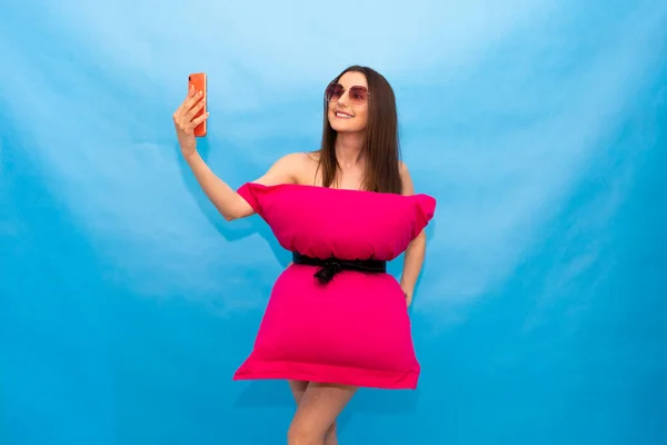 Mujer feliz en vestido de almohada rosa y gafas de sol haciendo foto selfie en el teléfono móvil para el desafío de almohada loco debido al aislamiento de la estancia en casa. Cuarentena del Caronavirus. Chica de moda. Llamada de almohada debido a casa —  Fotos de Stock