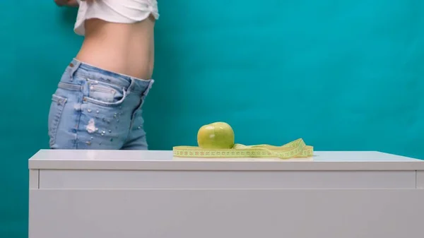 Weiblicher schlanker Bauch und grüner Apfel im Vordergrund, selektiver Fokus. Das Konzept der Gewichtsabnahme und der richtigen Ernährung — Stockfoto