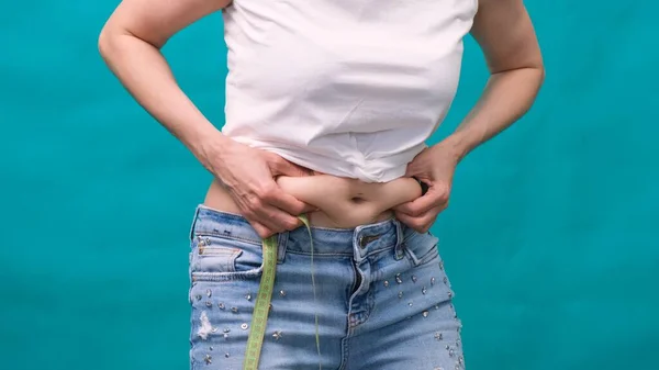 Frau hält eine Hautfalte auf einem dicken Bauch, fetter weiblicher Körper auf grünem Hintergrund. Kühne weibliche Taille. Das Konzept der Gewichtsabnahme und Ernährung. — Stockfoto