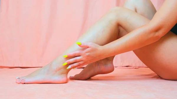 Gambe da donna in primo piano, ragazza che si accarezza le gambe con una crema rinfrescante sulle gambe isolate su uno sfondo rosa. concetto di cura della pelle. — Foto Stock