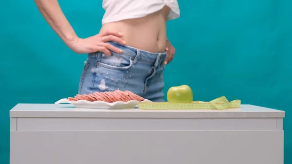 Frau wählt zwischen Apfel oder Wurst auf grünem Hintergrund. Das Konzept einer gesunden Ernährung, Ernährung und Willenskraft. — Stockfoto