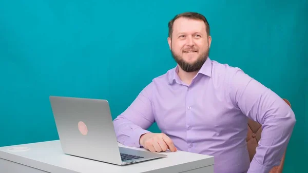 Jovem empresário feliz sorrindo e falando para a câmera. Retrato de um homem rindo enquanto olha para seu laptop. Homem trabalhando em sua mesa no escritório — Fotografia de Stock