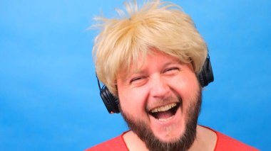 Peruklu, pembe tişörtlü, komik şişko adam kulaklıkla müzik dinliyor ve mavi arka planda dans ediyor.