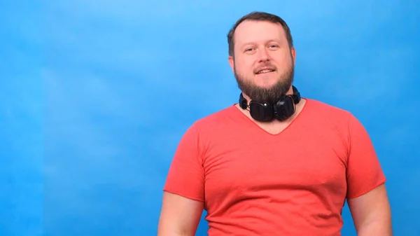 Barbudo engraçado bonitinho gordo homem em uma camiseta rosa escuta música e dança em um fundo azul, close-up, espaço de cópia . — Fotografia de Stock