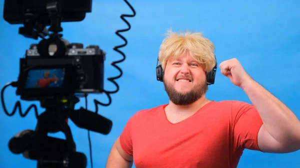 Причудливый толстяк в парике и розовой футболке ведет видеоблог на синем фоне. — стоковое фото