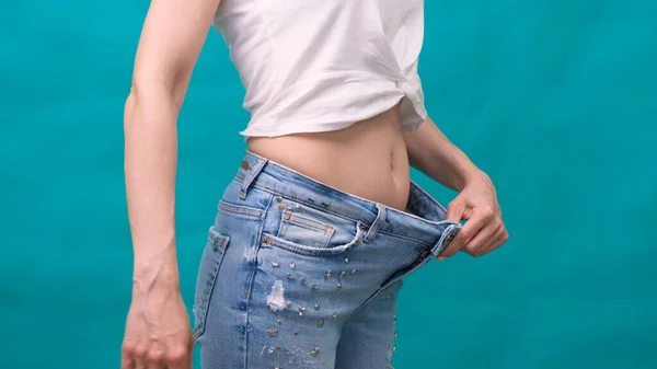 Привлекательная молодая женщина в джинсах и демонстрирует стройное тело после спортивных тренировок и здорового питания. Концепция потери веса. — стоковое фото
