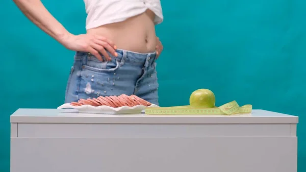Здоровый образ жизни, питание и спорт. Женщины держат медиатор между зеленым яблоком и колбасой . — стоковое фото