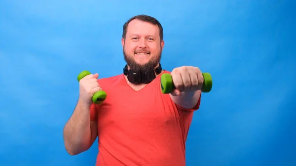 Schicker dicker Mann im rosafarbenen T-Shirt mit Hanteln macht lustige Übungen auf blauem Hintergrund — Stockfoto