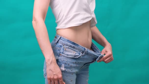 Atractiva mujer joven con pantalones vaqueros y mostrando cuerpo delgado después de entrenamientos deportivos y alimentación saludable. Concepto de pérdida de peso . — Vídeo de stock