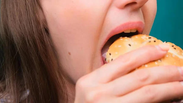 Feche de uma fêmea mordendo um hambúrguer em uma tela verde. O conceito de nutrição insalubre e dieta . — Fotografia de Stock