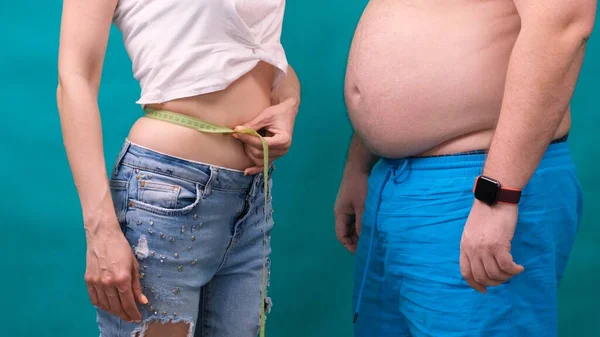 Pár dagadt férfi és vékony nő együtt állnak, mérőszalagba csomagolva. Táplálkozás, családfogyás és egészségügyi koncepció. — Stock Fotó