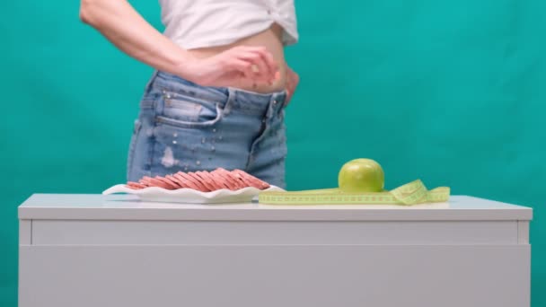 Женщина выбирает между яблоком или колбасой на зеленом фоне. Понятие здорового питания, диеты и силы воли . — стоковое видео