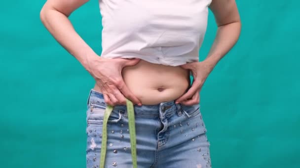 Vrouw houdt een huidplooi op een dikke buik, vet vrouwelijk lichaam op een groene achtergrond. Brutale vrouwelijke taille. Het concept van gewichtsverlies en dieet. — Stockvideo