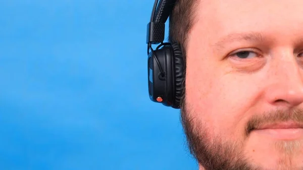 Barbudo divertido sonriente lindo gordo hombre en una camiseta rosa escucha música y baila sobre un fondo azul, primer plano, espacio de copia . —  Fotos de Stock