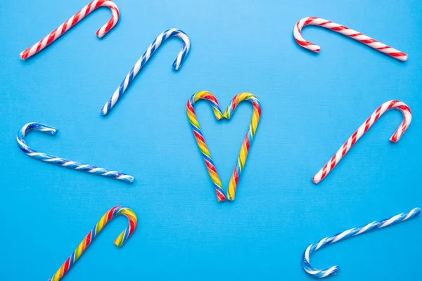 Muchos bastones de caramelo multicolores y un corazón sobre un fondo azul, espacio de copia — Foto de Stock