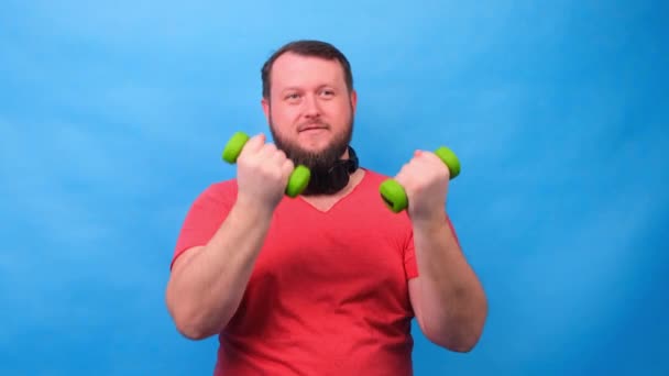 Fantasia maschile in una t-shirt rosa con manubri divertente facendo esercizi su uno sfondo blu — Video Stock
