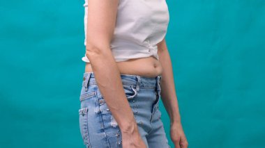 Kadının kalın bir karnı, yeşil arka planda şişman bir kadın vücudu var. Cesur kadın beli. Kilo kaybı ve diyet kavramı.