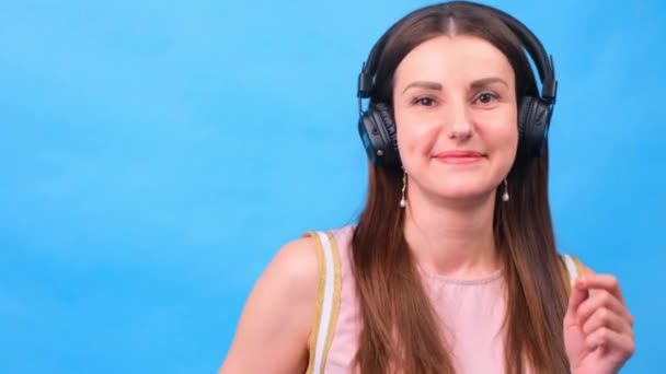 Kulaklıklı enerji kızı stüdyoda mavi bir arkaplanda müzik dinliyor. — Stok video