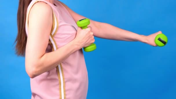 Graisse Femme en costume de sport rose avec haltères dans les mains fait des exercices sur un fond bleu. Le concept de sport, l'alimentation et la perte de poids. — Video