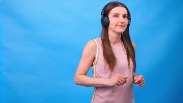 Beautiful Energy Girl with headphones listening to music on a blue background in the studio — Stock Video